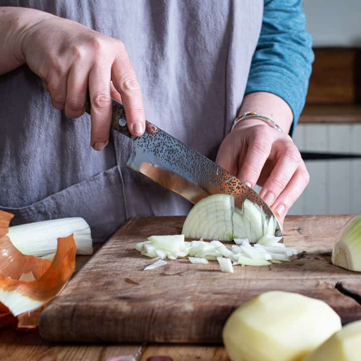 womans hands chopping an onion finely on a wooden chopping board