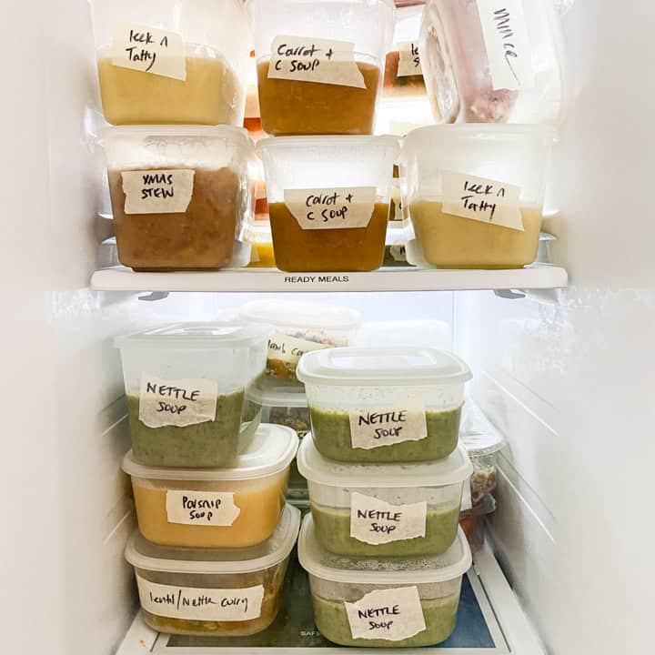 white freezer contents with various homemade soups and meal stacked in tupperware containers and all labelled with their contents