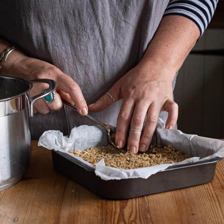 Womans pressing down flapjack mix in a grey metal baking tray