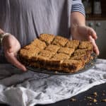 Woman in grey holding a metal plate filled with homemade date flapjack squares