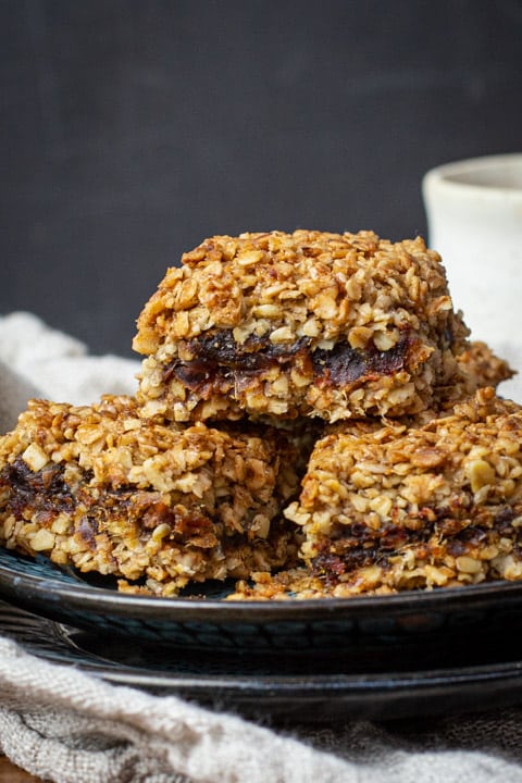 Three date flapjacks piled on a plate sitting on a cloth with a black background