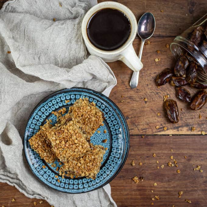 Ariel view of plate of flapjacks, cup of coffee, teaspoon and dates in a jar on a wooden table