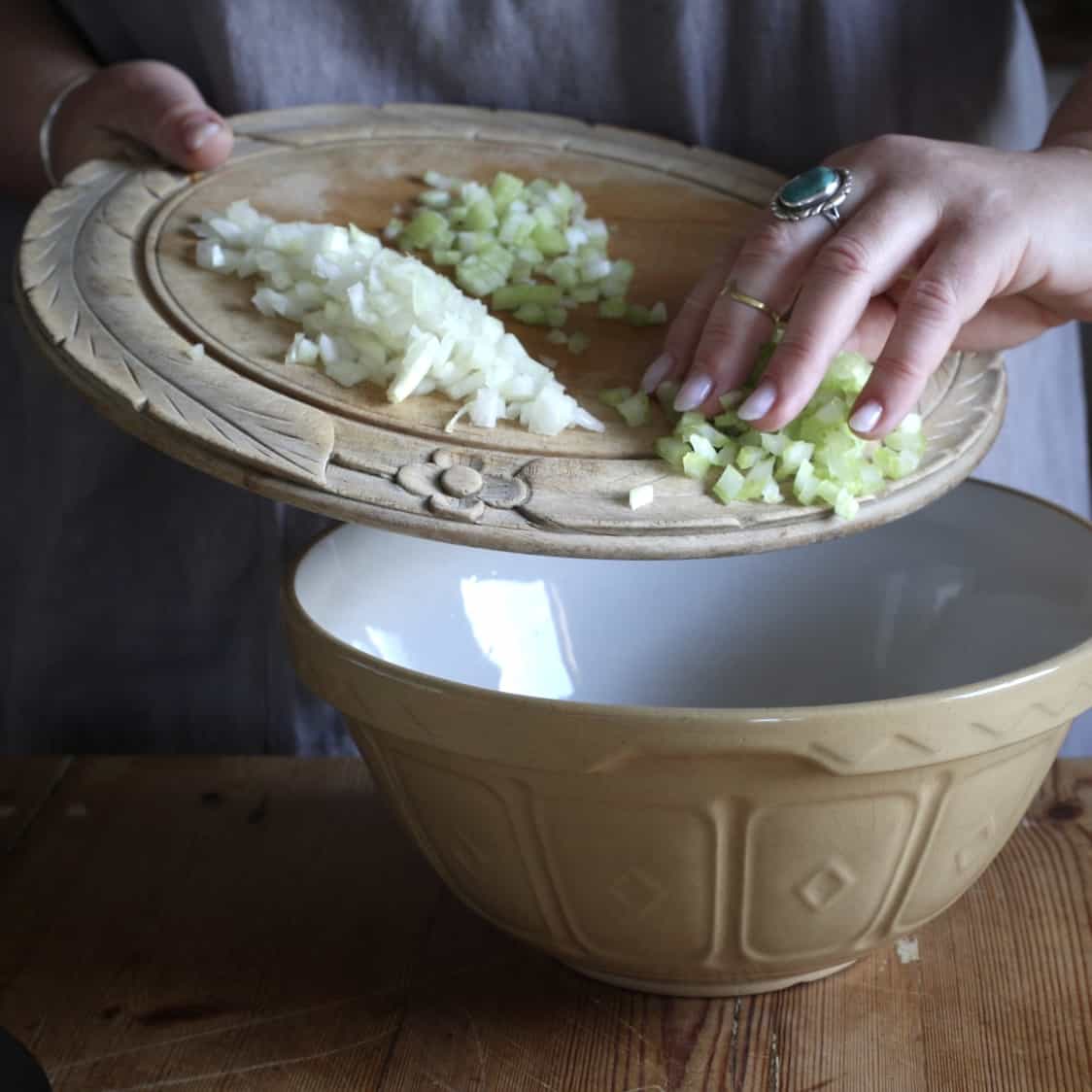 Woman sliding chopped veggies from a wooden board into a large mixing bowl