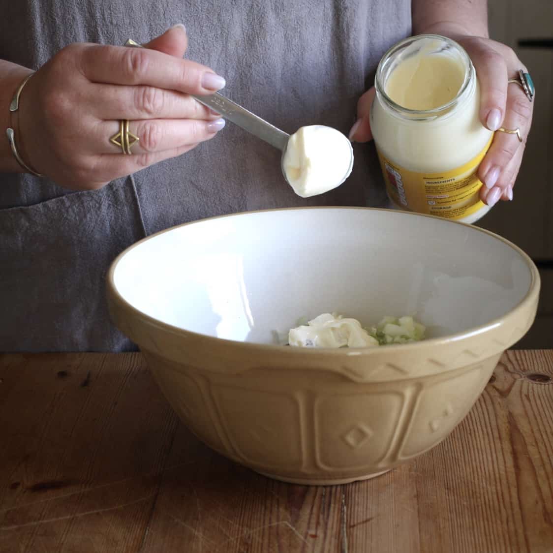 Woman hands holding a spoon of mayonnaise over a brown mixing bowl