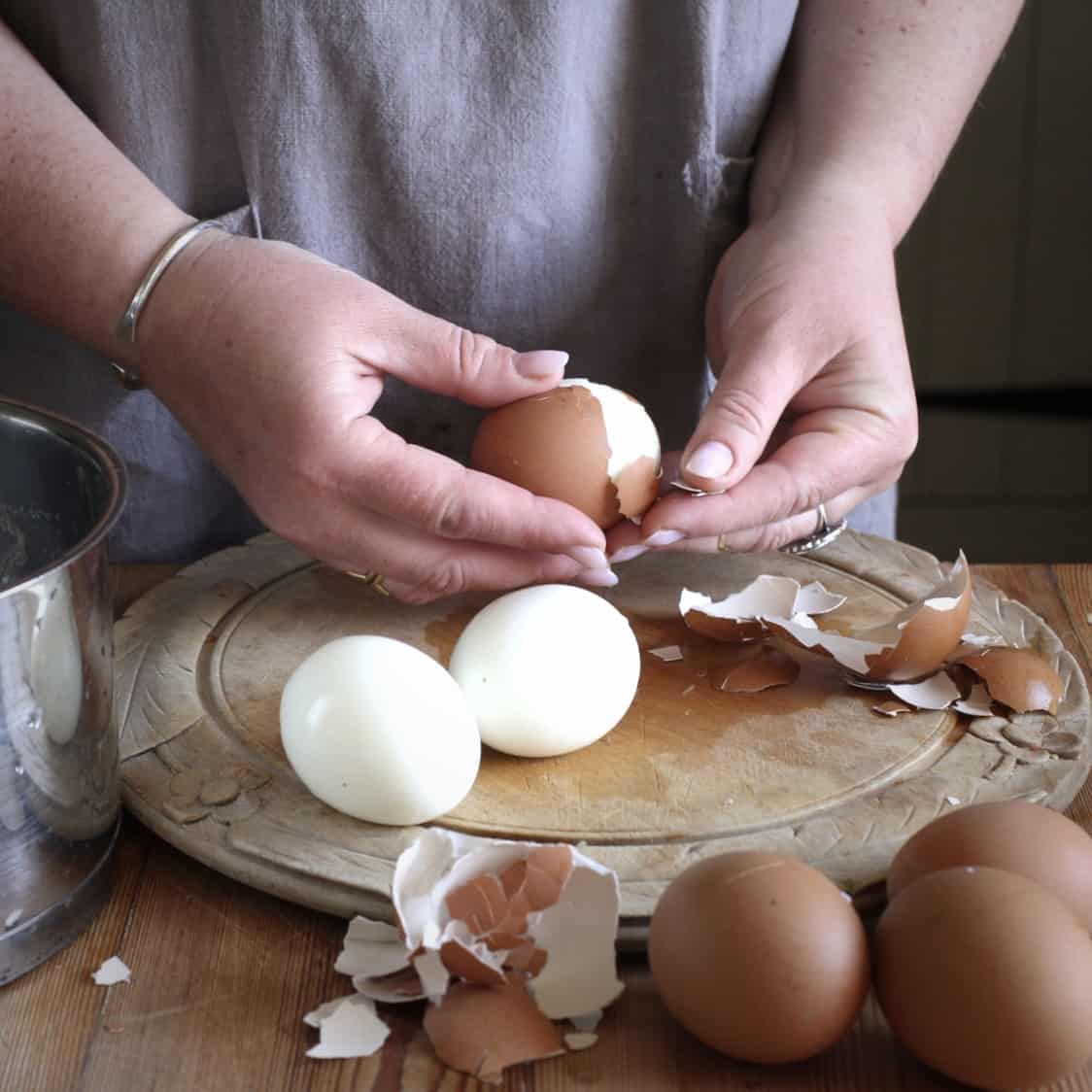 Woman peeling three hard boiled eggs on a rustic wooden chopping board