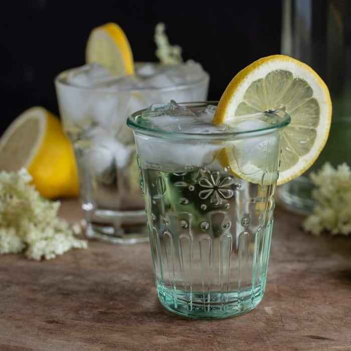 glass of homemade elderflower piled high with cordial, slices of lemon and ice