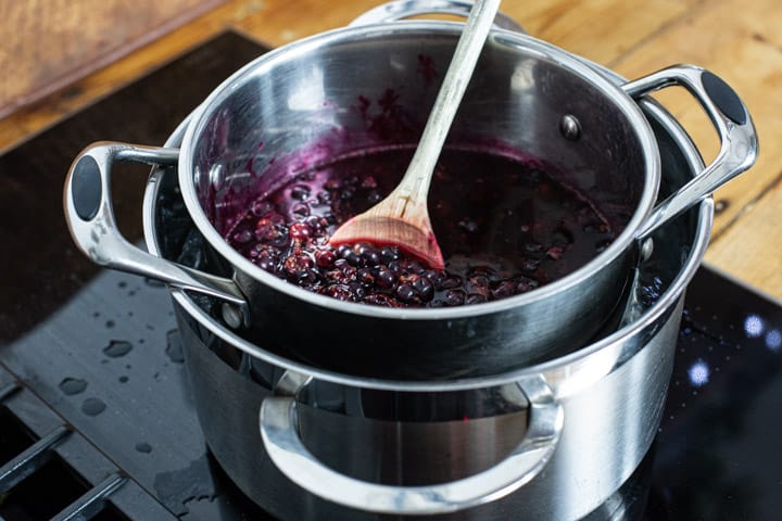 inside of a silver double boiler sowing gently stewed blackcurrants and a wooden spoon