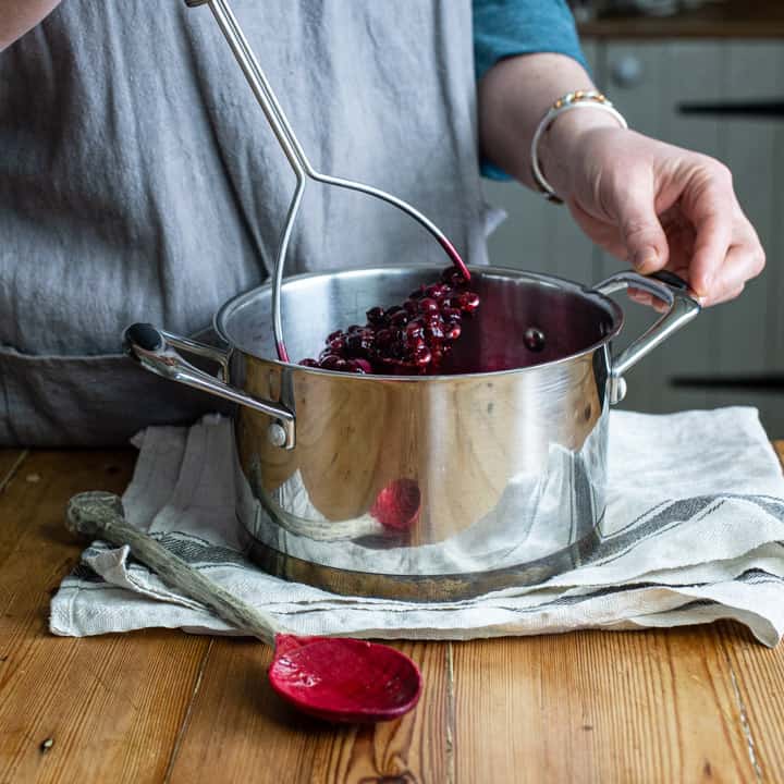 womans hands mashing a silver pan of blackcurrants to extract the juice