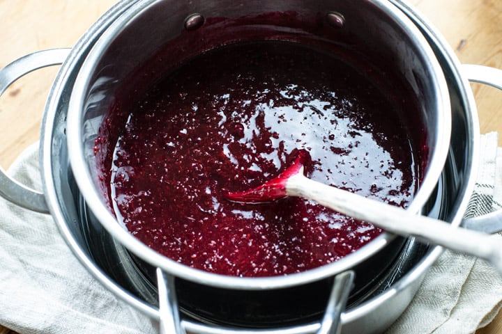 inside of a silver double boiler sowing gently stewed blackcurrants and a wooden spoon