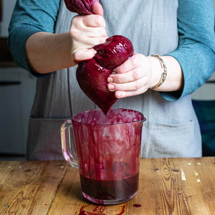 womans hands squeezing the juice from bag of blackcurrants into a glass jug