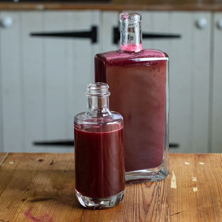 2 glass bottles on a rustic wooden counter filled with homemade blackcurrant syrup