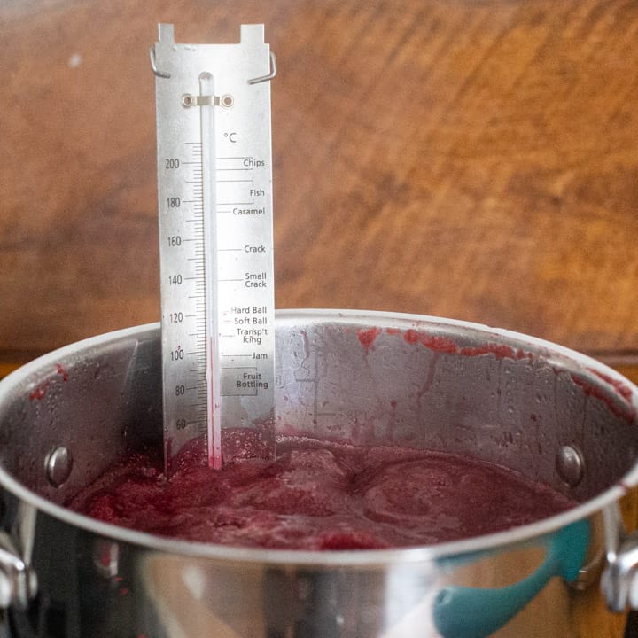 blackberry candy bubbling in a silver pan with a jam thermometer waiting to show hard crack stage