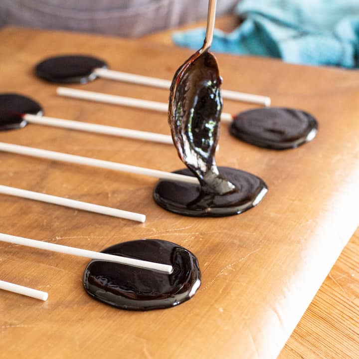 a teaspoon of blackberry candy syrup being poured over a white paper lollipop stick 