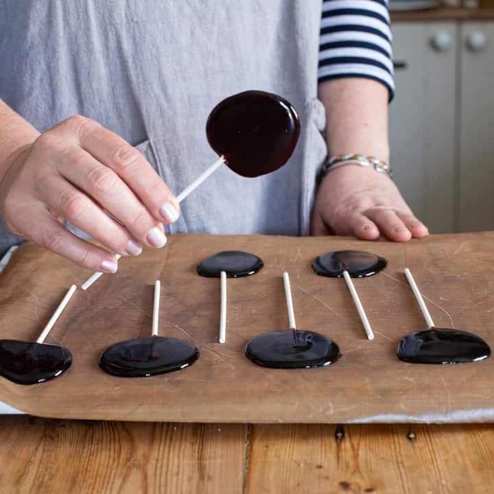 woman in grey holding up blackberry lollipop over a baking sheet of more lollipops