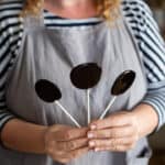 woman in grey holding three blackberry candies up by there white lollipop sticks