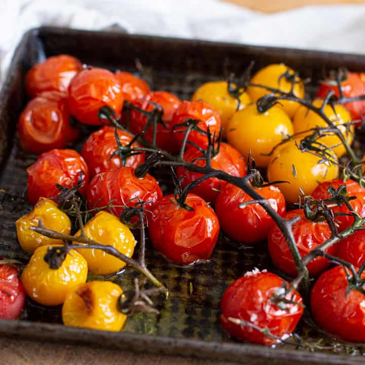 roasted red and yellow cherry tomatoes in a black baking tray on a wooden board