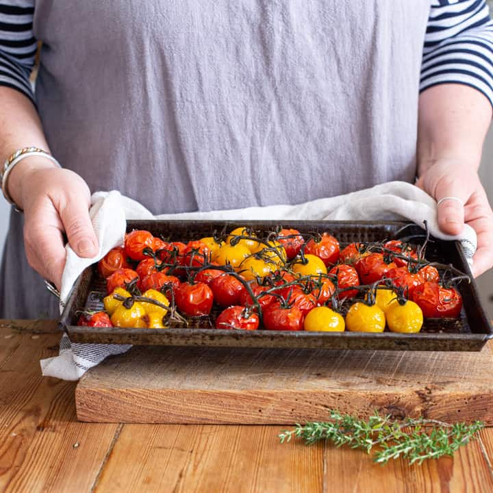 womans hands holding black tray of roasted red and yellow cherry tomatoes