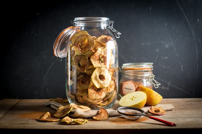 Glass jar filled with dried apple rings that have been dusted with cinnamon