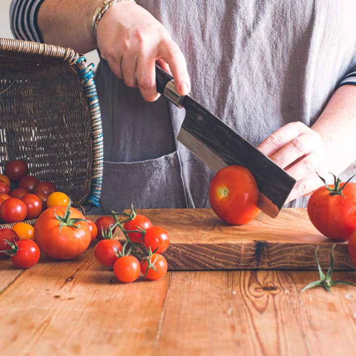 womans hands slicing red tomato on wooden chopping board