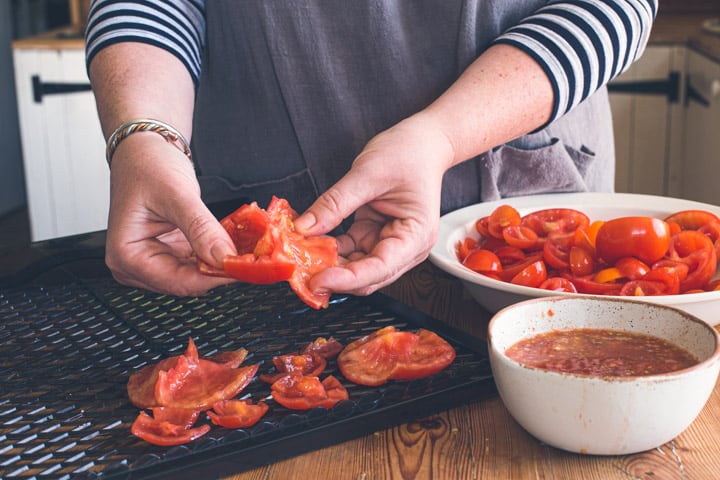 womans hands laying red tomatoes out on black dehydrator shelves on wooden surface for drying