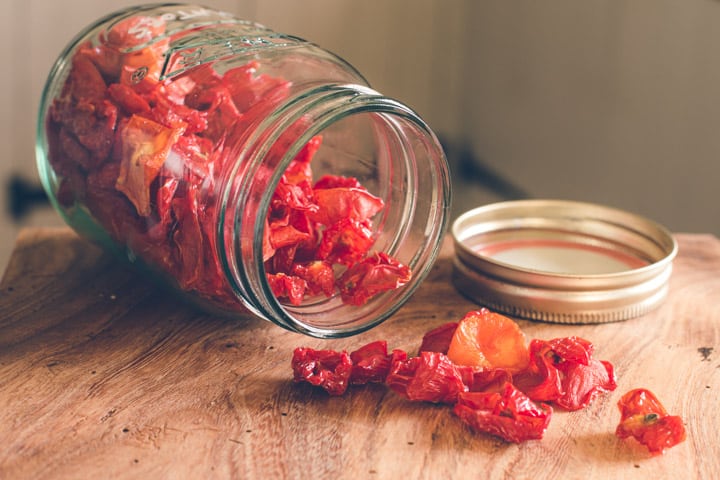 glass jar on wooden kitchen counter filled with dried cherry tomatoes