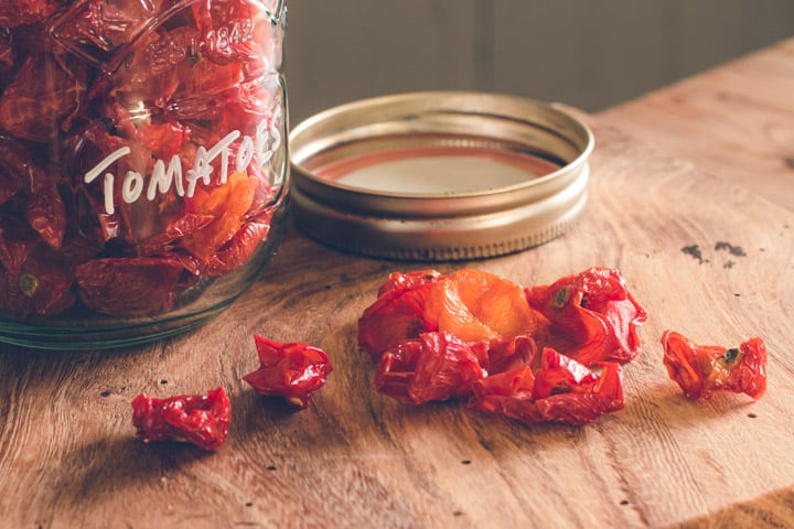 glass jar on wooden kitchen counter filled with dried cherry tomatoes