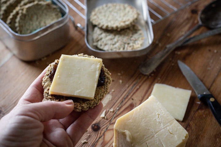 womans hands on wooden kitchen bench holding a freshly baked oatcake with a slice of cheese on