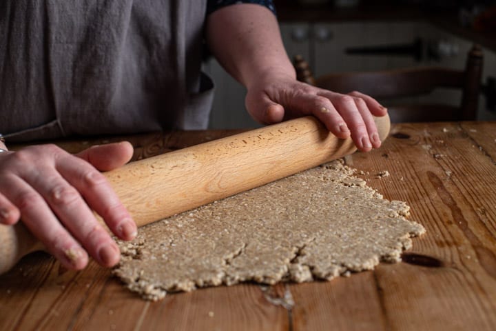 womans hands rolling out oatcake dough on a wooden counter