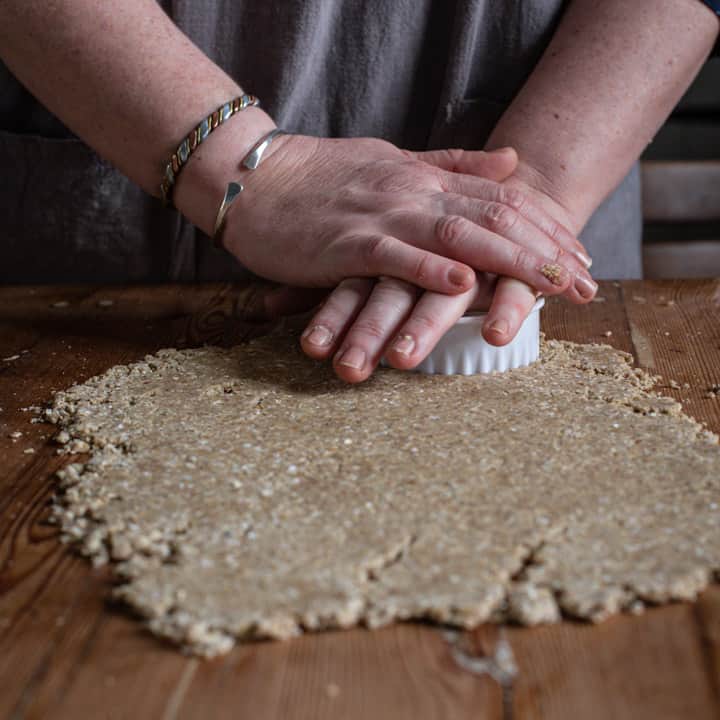 womans hands cutting oatcake dough with a white cookie cutter on a wooden counter