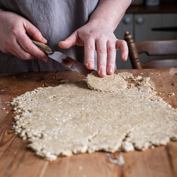 womans hands lifting an oatcake from the rolled out dough with a thin metal spatula