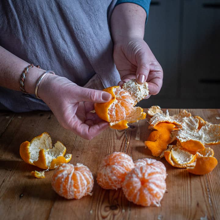 wooden kitchen counter with womans hands peeling satsumas ready to poach in red wine