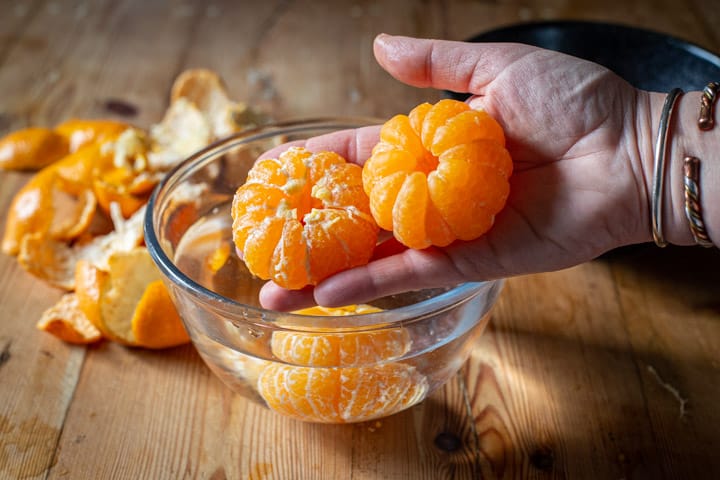 womans hand holding two satsumas that have been poached, and one which has had the pith removed too