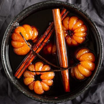 black bowl on grey background with poached satsumas, red wine syrup, cinnamon sticks and a vanilla pod