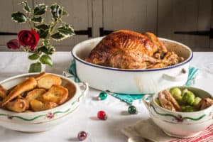 White table cloth with enamel roasting pan with roast chicken and white bowls of parsnips and Brussels sprouts