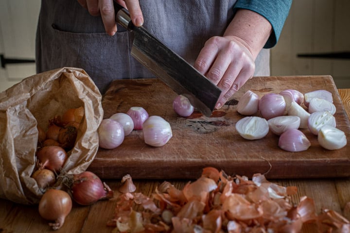 womans hands slicing shallots on a wooden counter