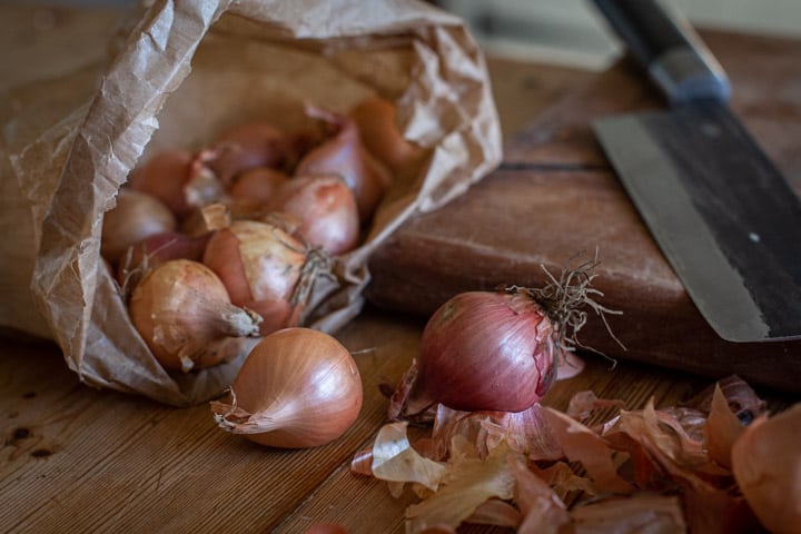 pretty pink shallots spilling from a brown paper bag onto a wooden chopping board