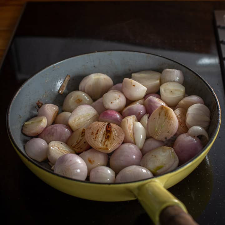 yellow enamel frying pan on a black stove top with several shallots inside cooking