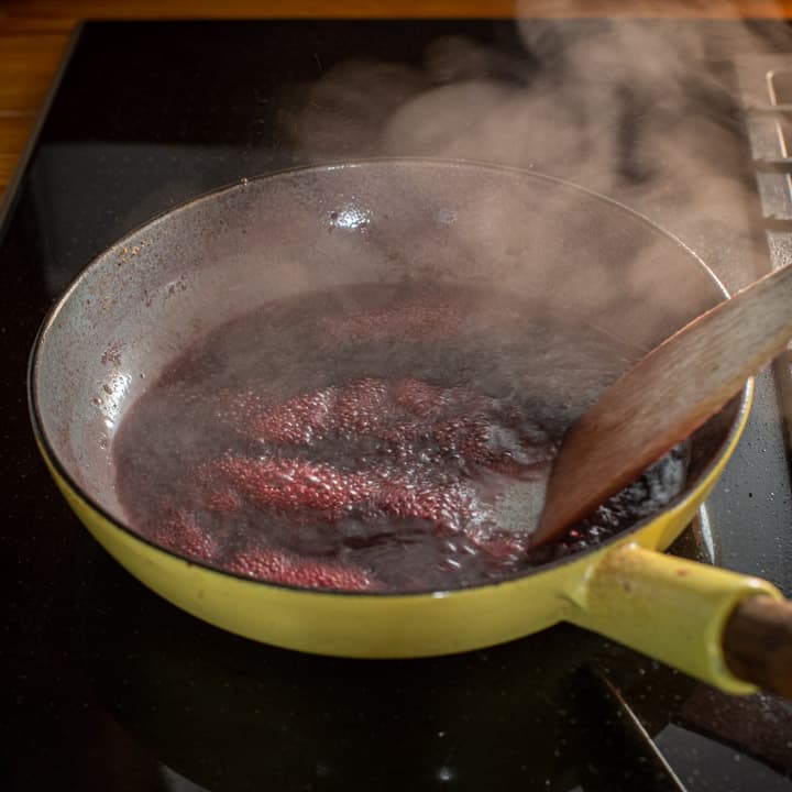 yellow enamel frying pan on a black stove top with red wine boiling and the bottom of the pan being scraped with a wooden spatula