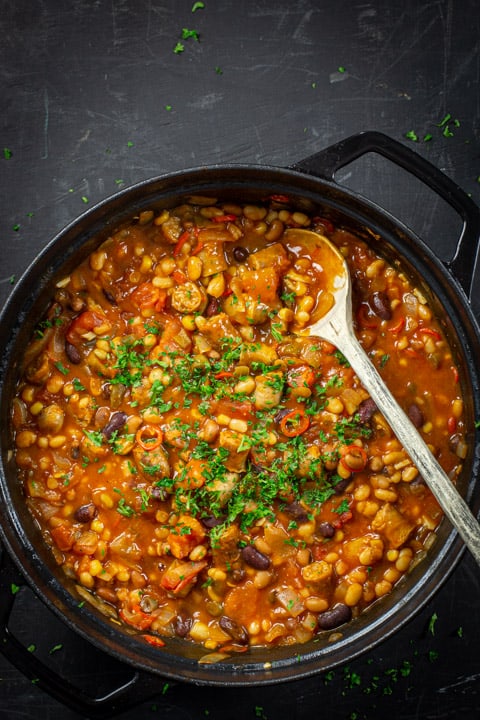 Pan of cowboy stew with wooden spoon on a black background