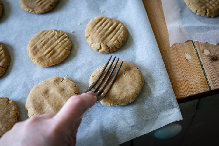 womans hand pressing a fork into ginger cookie dough before baking