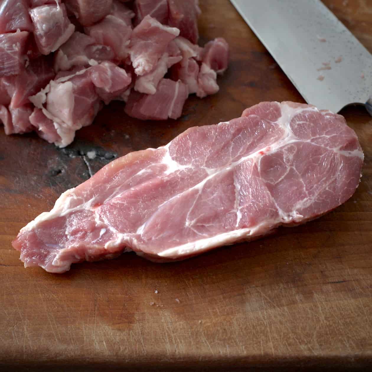 Slice of raw pork on a wooden chopping board with a sharp knife behind 