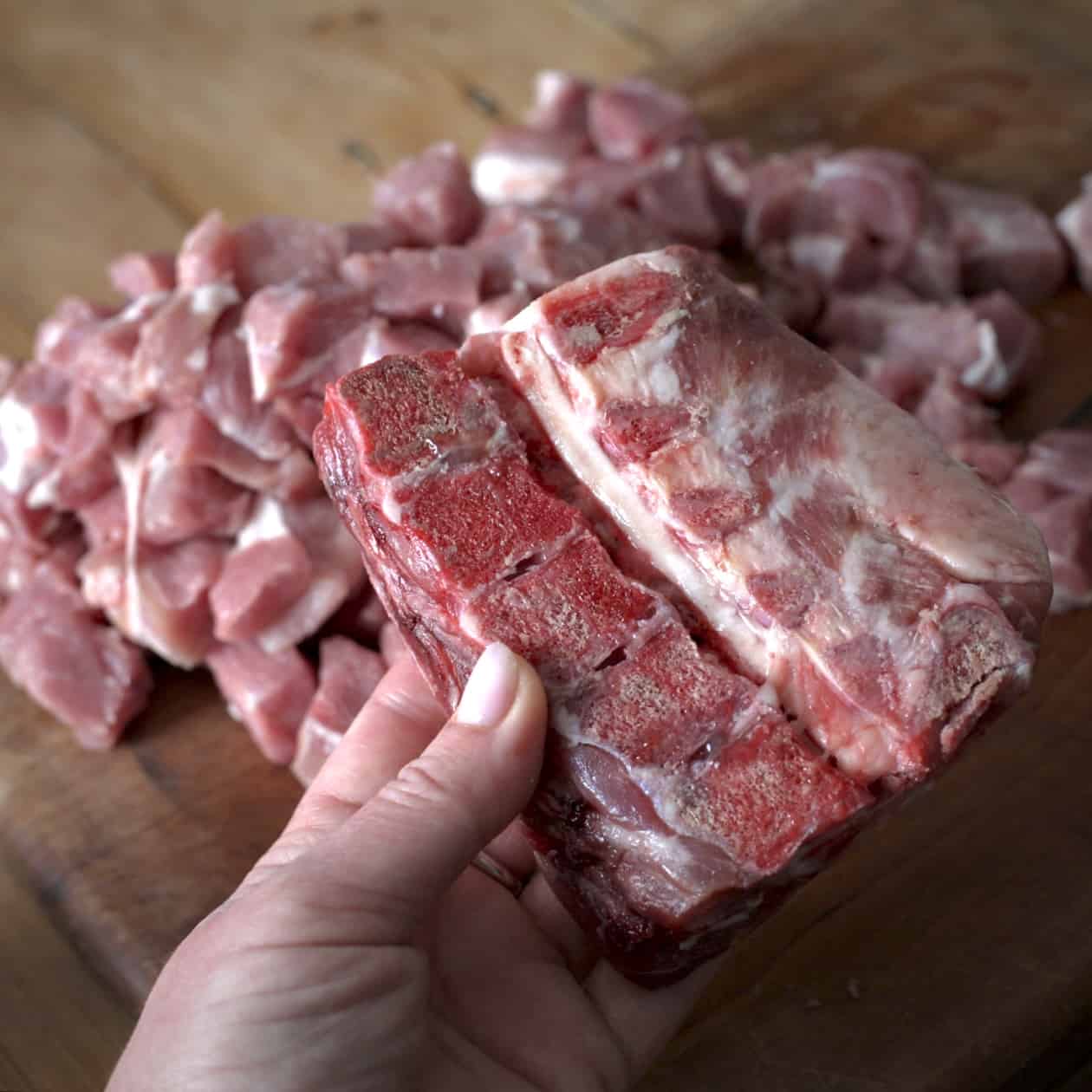 Woman’s holding a raw pork bone over a pile of dice pork on a wooden board