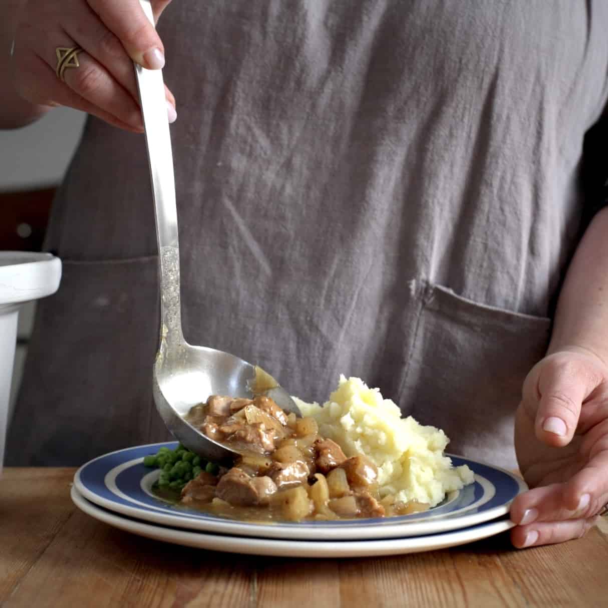 Woman’s serving up slow cooker pork in cider from s white slow cooker pot onto a blue and white plate