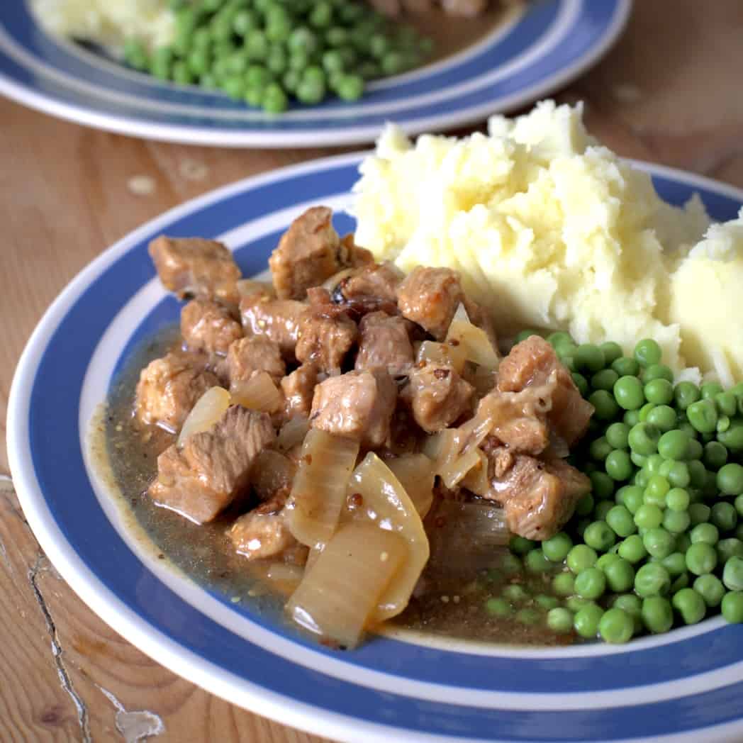 A blue and white plate with buttery mashed potato, green peas and pork in coder