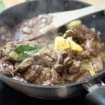 black frying pan with veniosn livers cooking along with bay leaves and onion