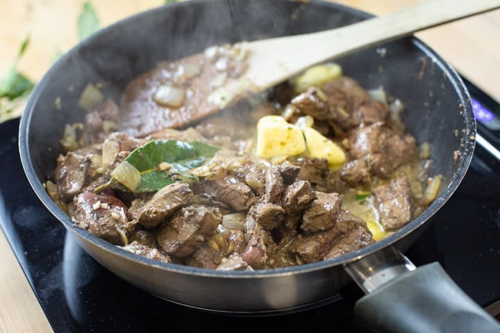 black frying pan with veniosn livers cooking along with bay leaves and onion