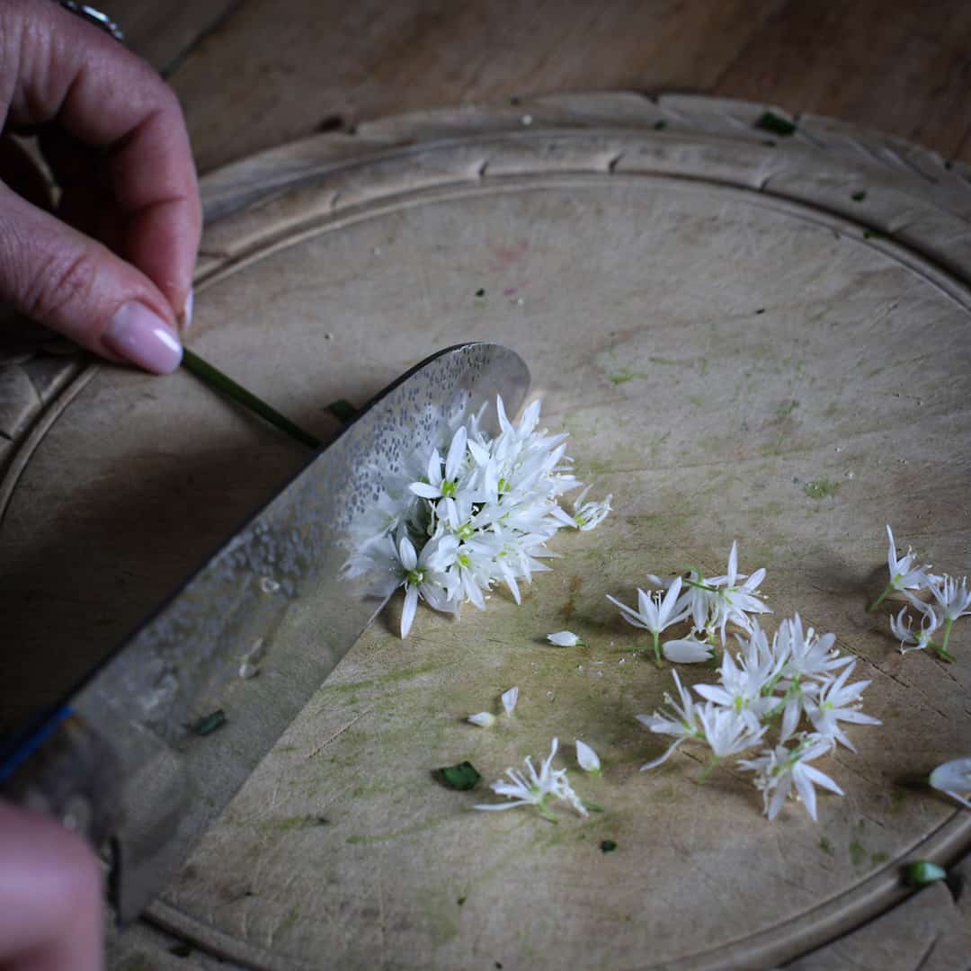Wild garlic flowers being cut from the stem on an old fashioned wooden chopping board