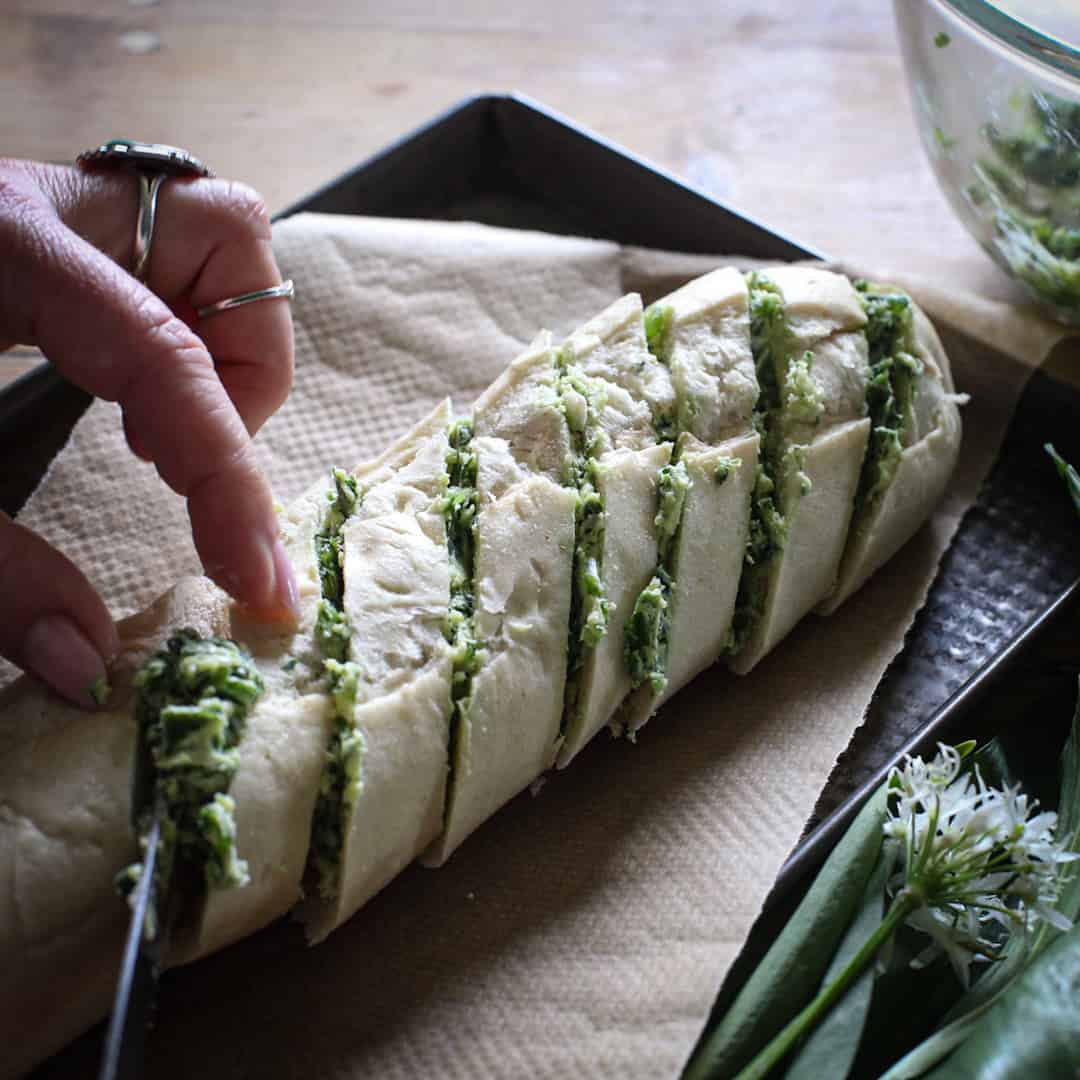Womans hands spreading a small baguette with wild garlic butter