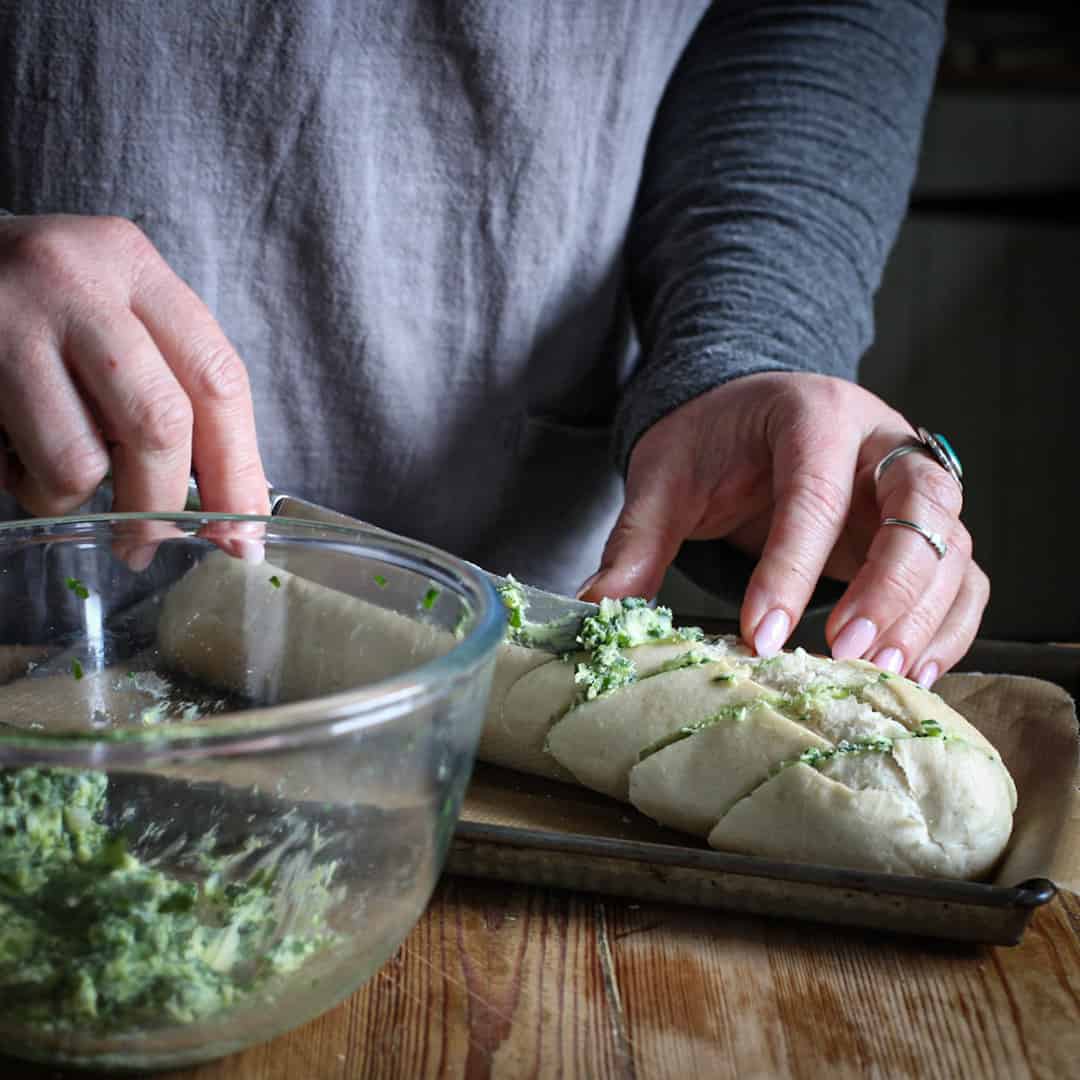 Womans hands spreading bright green wild garlic butter onto a part baked baguette