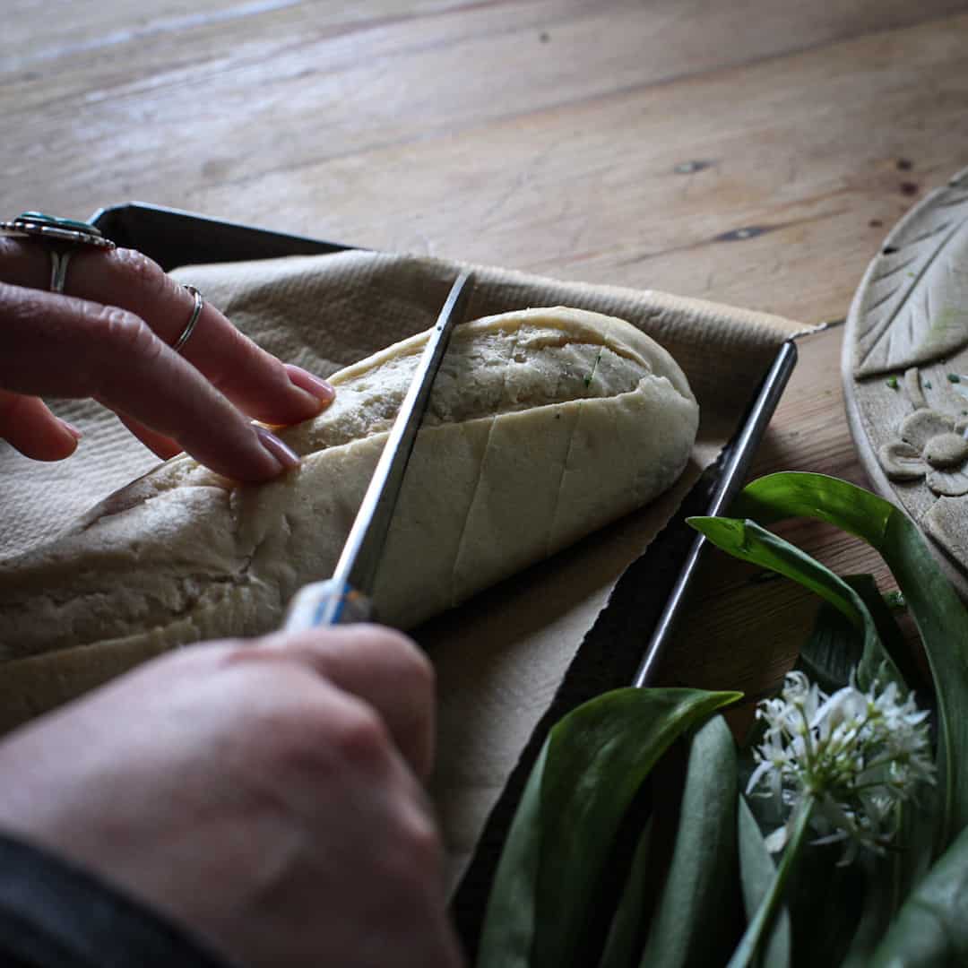 Woman slicing an unbaked baguette with a silver knife